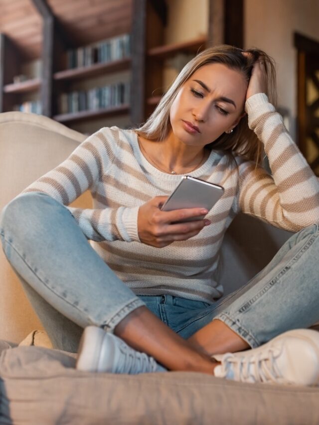 Worried,Lady,Looking,At,Smartphone,Screen,,Sitting,On,Couch,At
