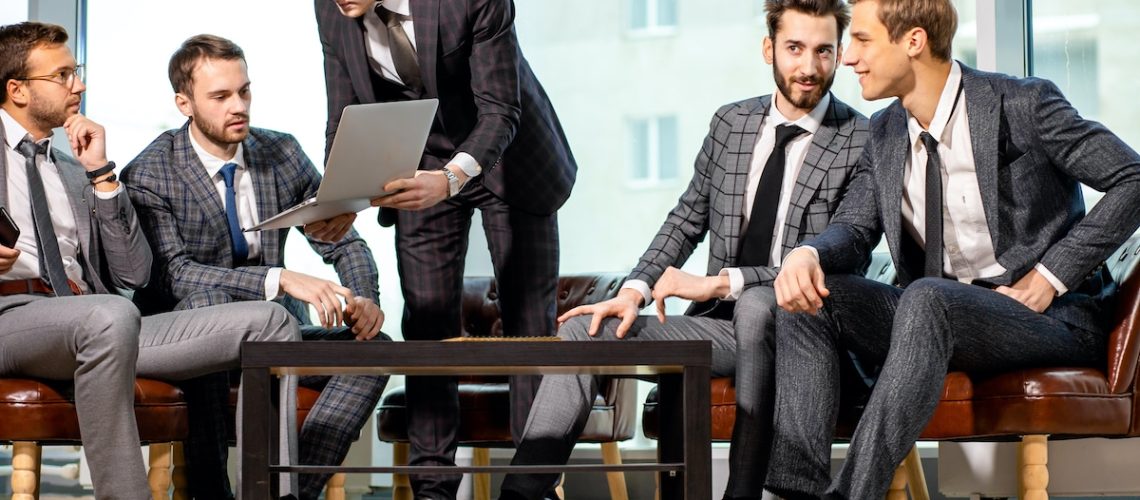 togetherness and partnership of young caucasian business men at work, group of men in tuxedo isolated in modern office, gathered to have discussion, conversation